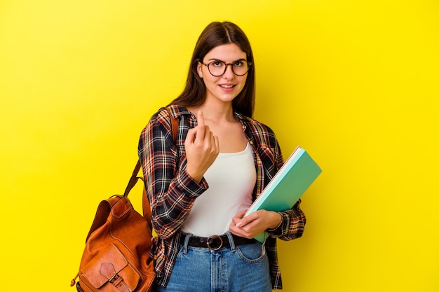 Mujer joven estudiante en amarillo apuntando con el dedo como si invitara a acercarse.