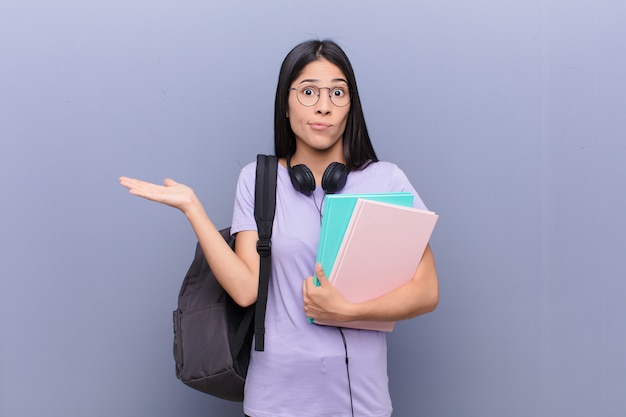 Mujer joven estudiante bastante latino contra la pared gris