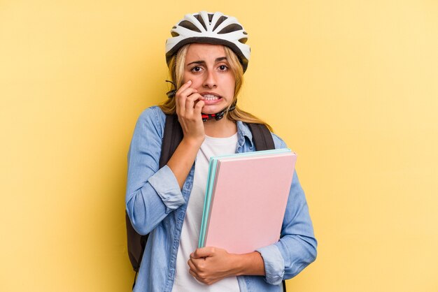 Mujer joven estudiante caucásica con un casco de bicicleta aislado sobre fondo amarillo mordiéndose las uñas, nervioso y muy ansioso.