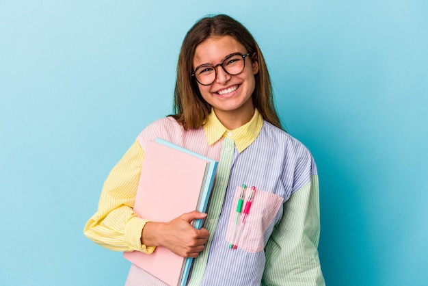 Mujer joven estudiante caucásica sosteniendo libros aislados sobre fondo azul feliz, sonriente y alegre.