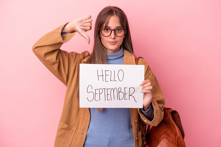 Foto mujer joven estudiante caucásica sosteniendo pancarta hola septiembre aislado sobre fondo rosa mostrando un gesto de aversión, pulgares hacia abajo. concepto de desacuerdo.