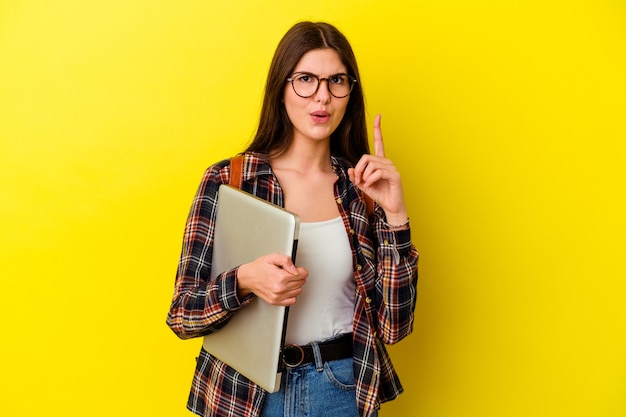 Mujer joven estudiante caucásica sosteniendo un portátil aislado sobre fondo rosa con una gran idea, concepto de creatividad.