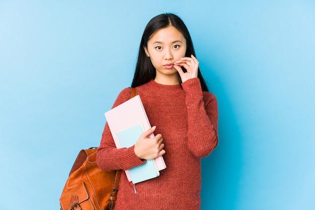 Mujer joven estudiante chino aislado con los dedos en los labios manteniendo un secreto.