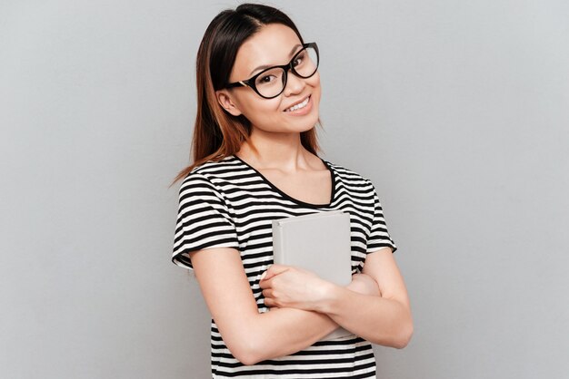 Mujer joven estudiante con gafas con portátil mirando a cámara
