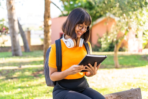 Mujer joven estudiante ganar un parque sosteniendo un cuaderno