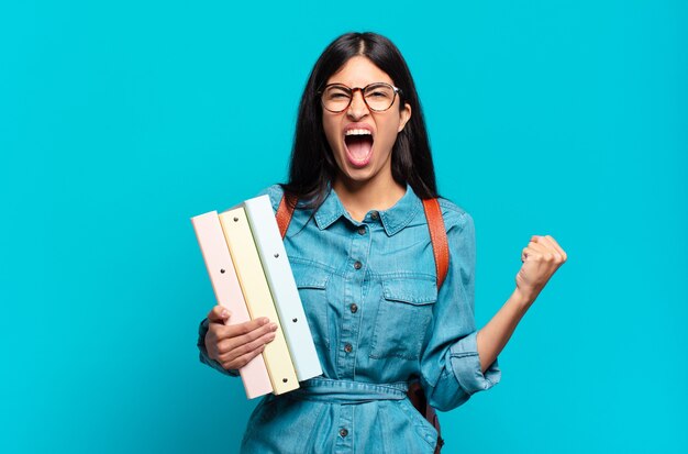 Mujer joven estudiante hispana gritando agresivamente con una expresión enojada o con los puños apretados celebrando el éxito