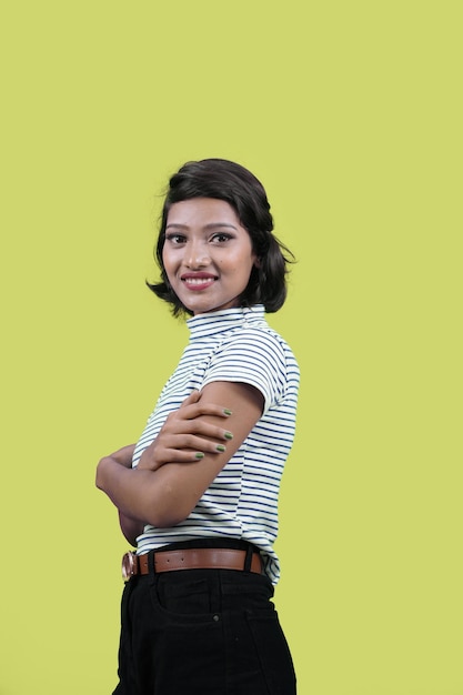 Mujer joven estudiante india sonriendo confiada con los brazos cruzados mirando a la cámara sobre la pared amarilla