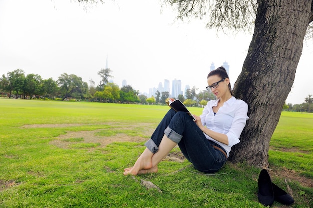 Mujer joven estudiante leyendo un libro y estudiando en el parque