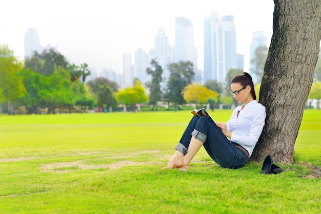 Mujer joven estudiante leyendo un libro y estudiando en el parque