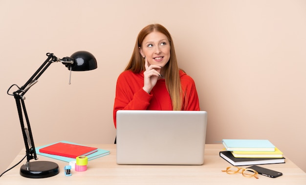 Mujer joven estudiante en un lugar de trabajo con un portátil pensando en una idea mientras mira hacia arriba