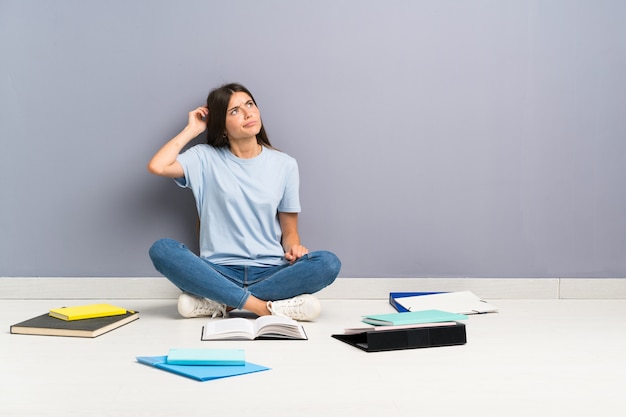 Mujer joven estudiante con muchos libros en el piso que tiene dudas y con expresión de la cara confusa