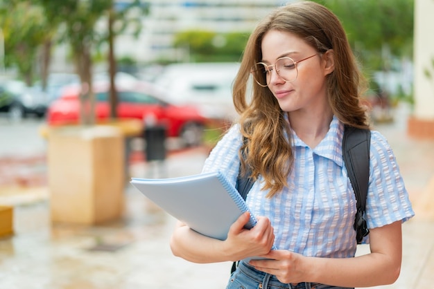 Mujer joven estudiante pelirroja al aire libre con expresión feliz