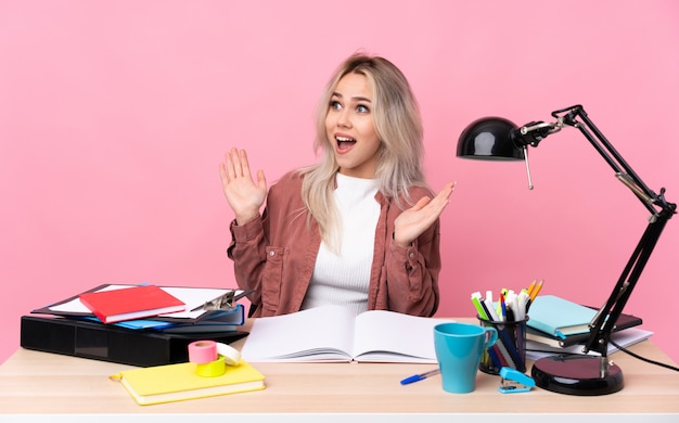 Mujer joven estudiante que trabaja en una mesa con expresión facial sorpresa