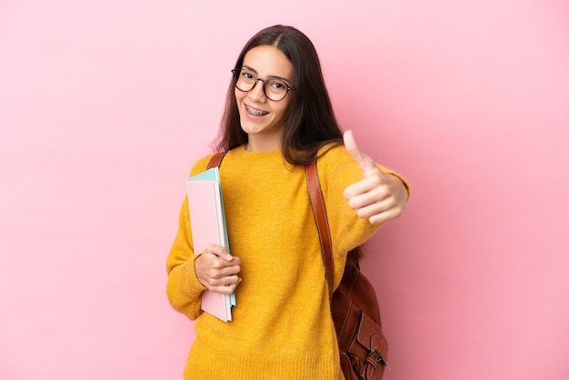 Mujer joven estudiante sobre antecedentes aislados con los pulgares hacia arriba porque algo bueno ha sucedido