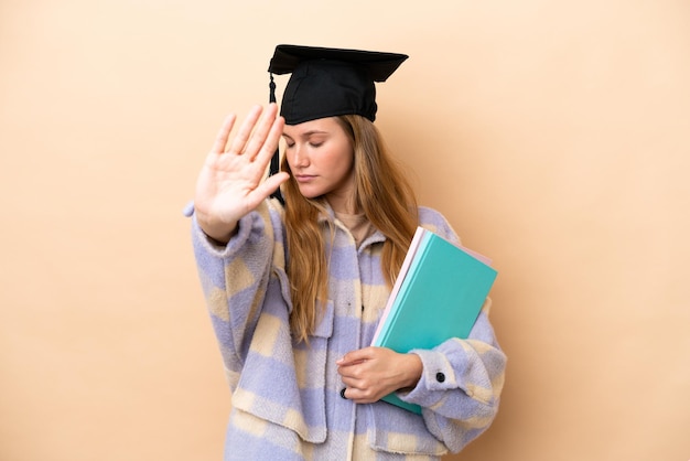 Mujer joven estudiante sobre fondo aislado haciendo gesto de parada y decepcionado