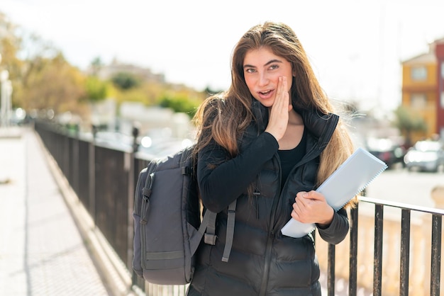 Mujer joven estudiante sobre fondo aislado susurrando algo