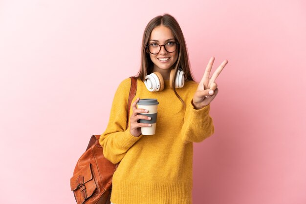 Mujer joven estudiante sobre fondo rosa aislado sonriendo y mostrando el signo de la victoria