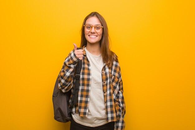 Mujer joven estudiante sonriendo y levantando el pulgar hacia arriba