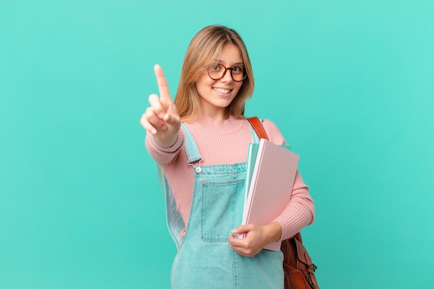 Mujer joven estudiante sonriendo con orgullo y confianza haciendo el número uno