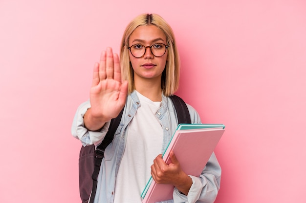 Mujer joven estudiante venezolana aislada en la pared rosa de pie con la mano extendida mostrando la señal de stop, impidiéndole