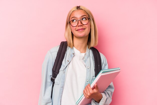 Mujer joven estudiante venezolana aislada en la pared rosada soñando con lograr metas y propósitos