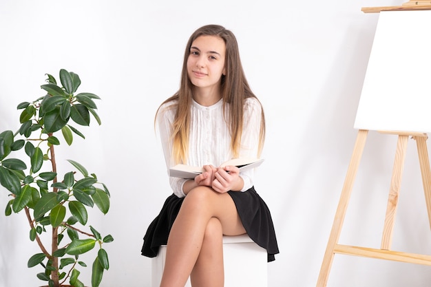 Mujer joven en estudio de arte con libro sobre fondo blanco.