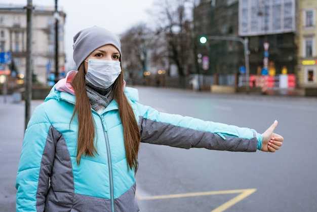 Una mujer joven de etnia caucásica con una chaqueta y un sombrero abrigados se encuentra en la calle con una máscara se detiene ...