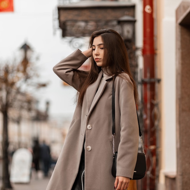 Mujer joven europea en un abrigo gris de moda en una calle de la ciudad en un día de otoño