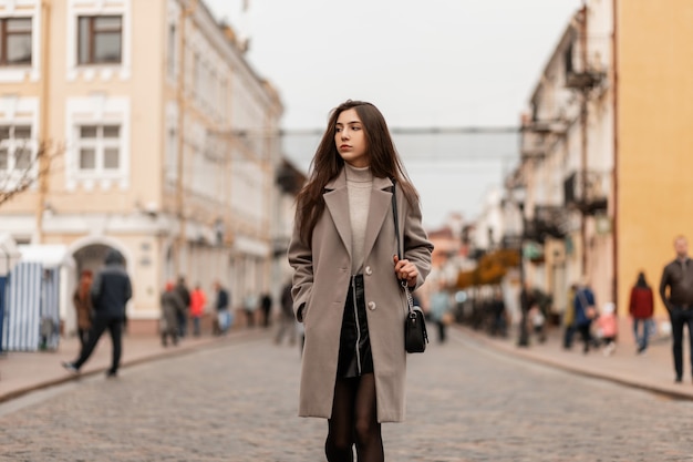 Mujer joven europea en un abrigo gris de moda en una calle de la ciudad en un día de otoño