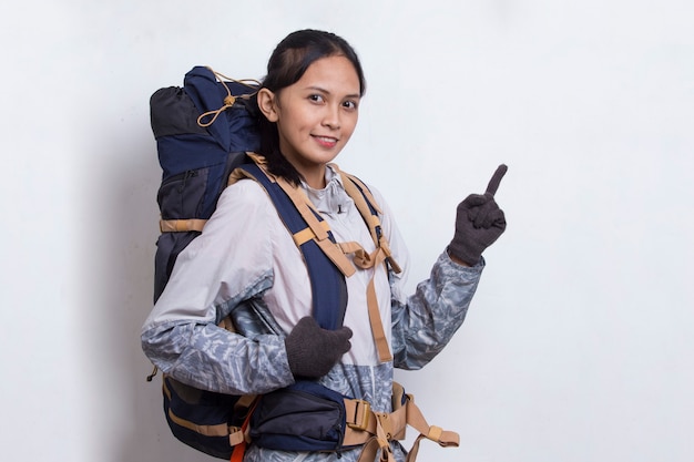 Mujer joven excursionista asiática con mochila dedo acusador en el espacio vacío sobre fondo blanco.