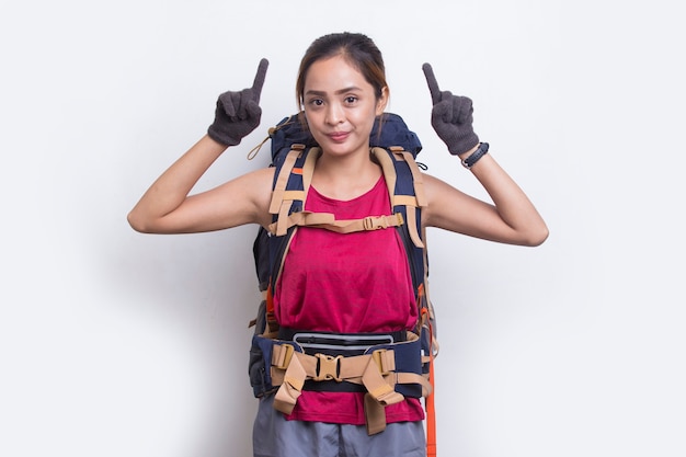 Mujer joven excursionista asiática con mochila dedo acusador en el espacio vacío sobre fondo blanco.