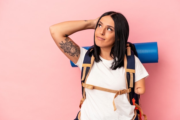 Mujer joven excursionista caucásica con un brazo aislado sobre fondo rosa tocando la parte posterior de la cabeza, pensando y haciendo una elección.