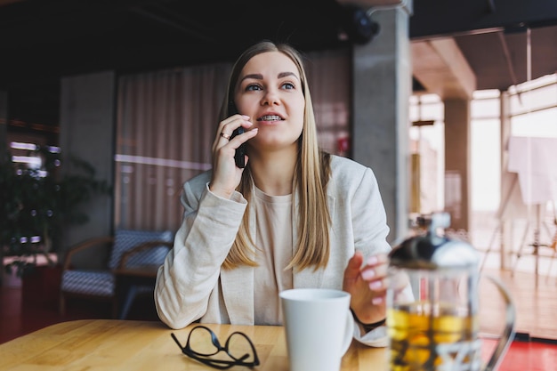 Mujer joven exitosa resolviendo problemas de negocios durante una conversación telefónica sentada en un café moderno y trabajando con una computadora portátil Lindo interior está disfrutando de su tiempo libre en el café