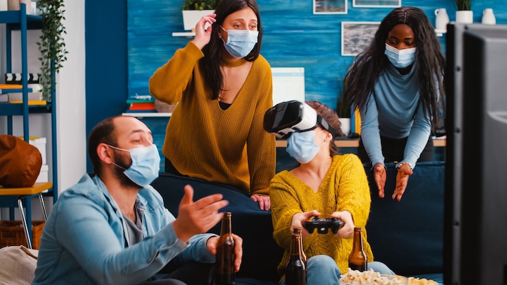Foto mujer joven experimentando realidad virtual jugando videojuegos con auriculares vr y joystick en la sala de estar de su casa mientras sus amigos la apoyan para mantener el distanciamiento social debido a la pandemia global