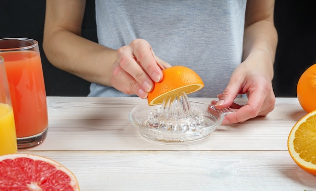 Mujer joven exprime jugo de naranja con un exprimidor de vidrio manual