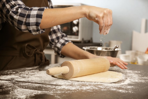 Mujer joven extendiendo la masa en la cocina