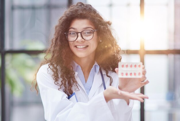 Mujer joven farmacéutica sosteniendo pastillas mientras está sentada en la mesa en la oficina