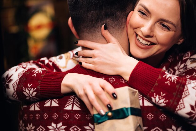 Mujer joven feliz abrazando a su novio y abrazándolo cerca del árbol de abeto brillante decorado romántico