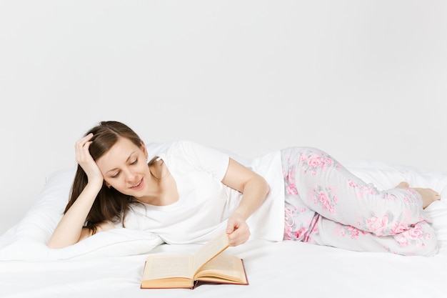 Mujer joven feliz acostado en la cama con sábana blanca, almohada, manta en la pared blanca