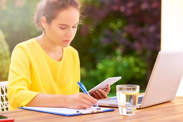 Mujer joven feliz aprendiendo en casa y usando una computadora portátil al aire libre en el jardín