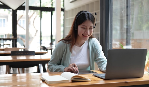 Mujer joven feliz en auriculares hablando mirando la computadora portátil haciendo notas estudiante hablando por videoconferencia profesora entrenadora tutoría por cámara web formación en línea ecoaching conceptxA