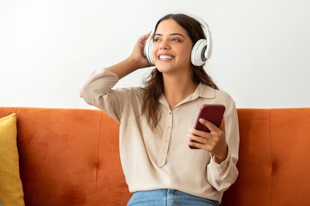 Mujer joven feliz con auriculares inalámbricos escuchando música en su teléfono inteligente en casa