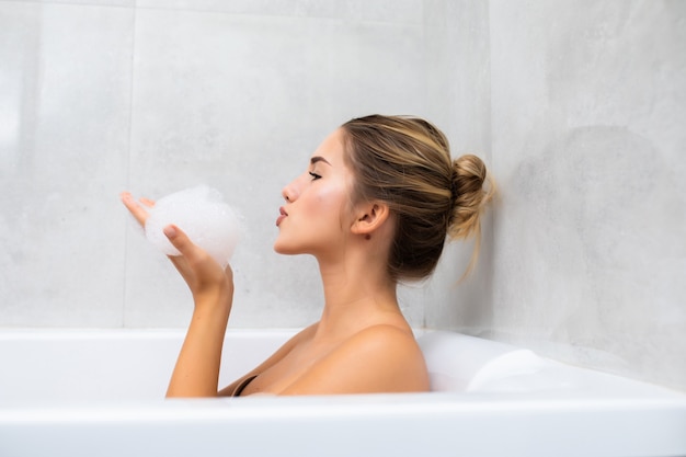 Mujer joven feliz en la bañera jugando con espuma