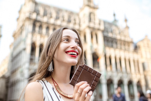 Mujer joven y feliz con barra de chocolate negro de pie al aire libre en la Grand Place de Bruselas en Bélgica. Bélgica es famosa por su chocolate