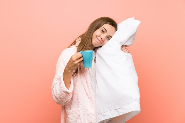 Mujer joven feliz en la bata sobre la pared rosada que sostiene una taza de café