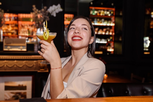 Mujer joven feliz bebe un cóctel sentado en una barra de bar