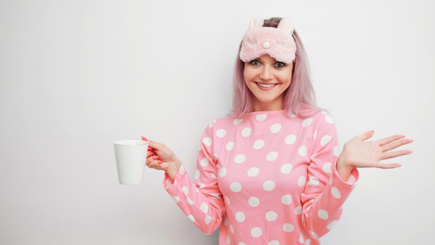 Mujer joven feliz beber café por la mañana. Hermosa chica en pijama rosa y máscara para dormir