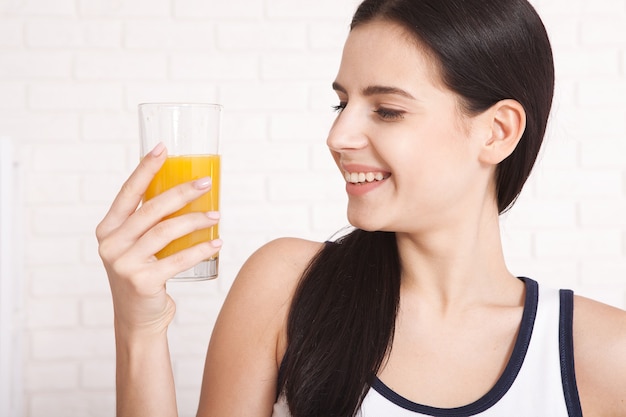 Mujer joven feliz bebiendo jugo de naranja en casa