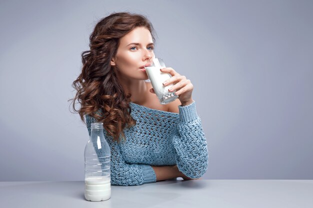 Mujer joven feliz bebiendo leche sobre espacio gris