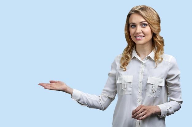 Mujer joven feliz en blusa blanca mostrando algo con las manos sobre fondo de color